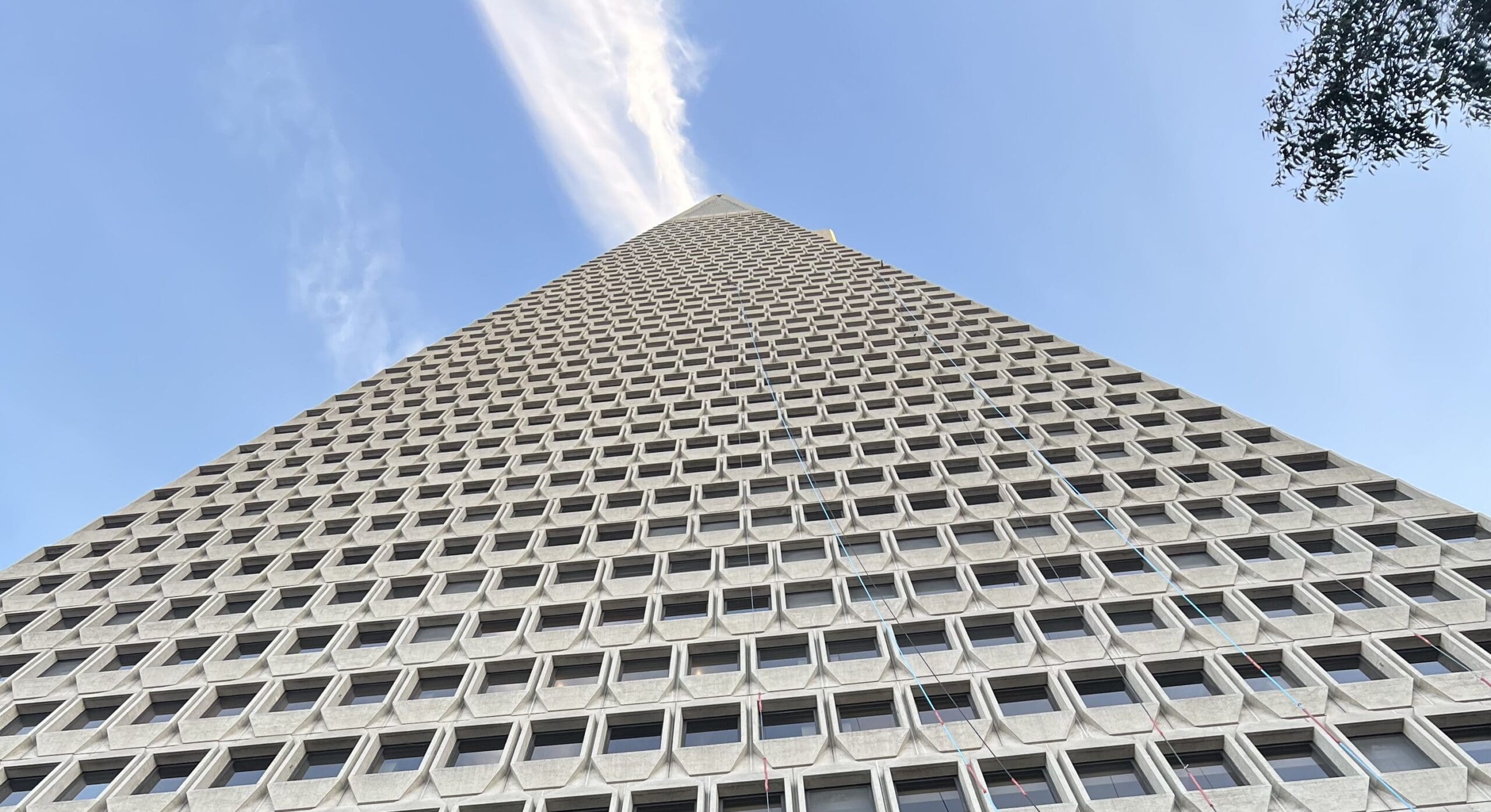 Looking up from the base of the Transamerica Pyramid, its geometric facade of repeating windows stretches up into the blue sky.